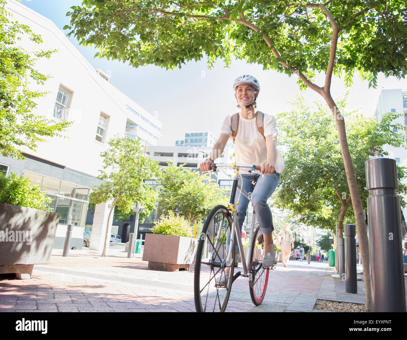 Smiling young woman with helmet riding bicycle in urban park Stock Photo