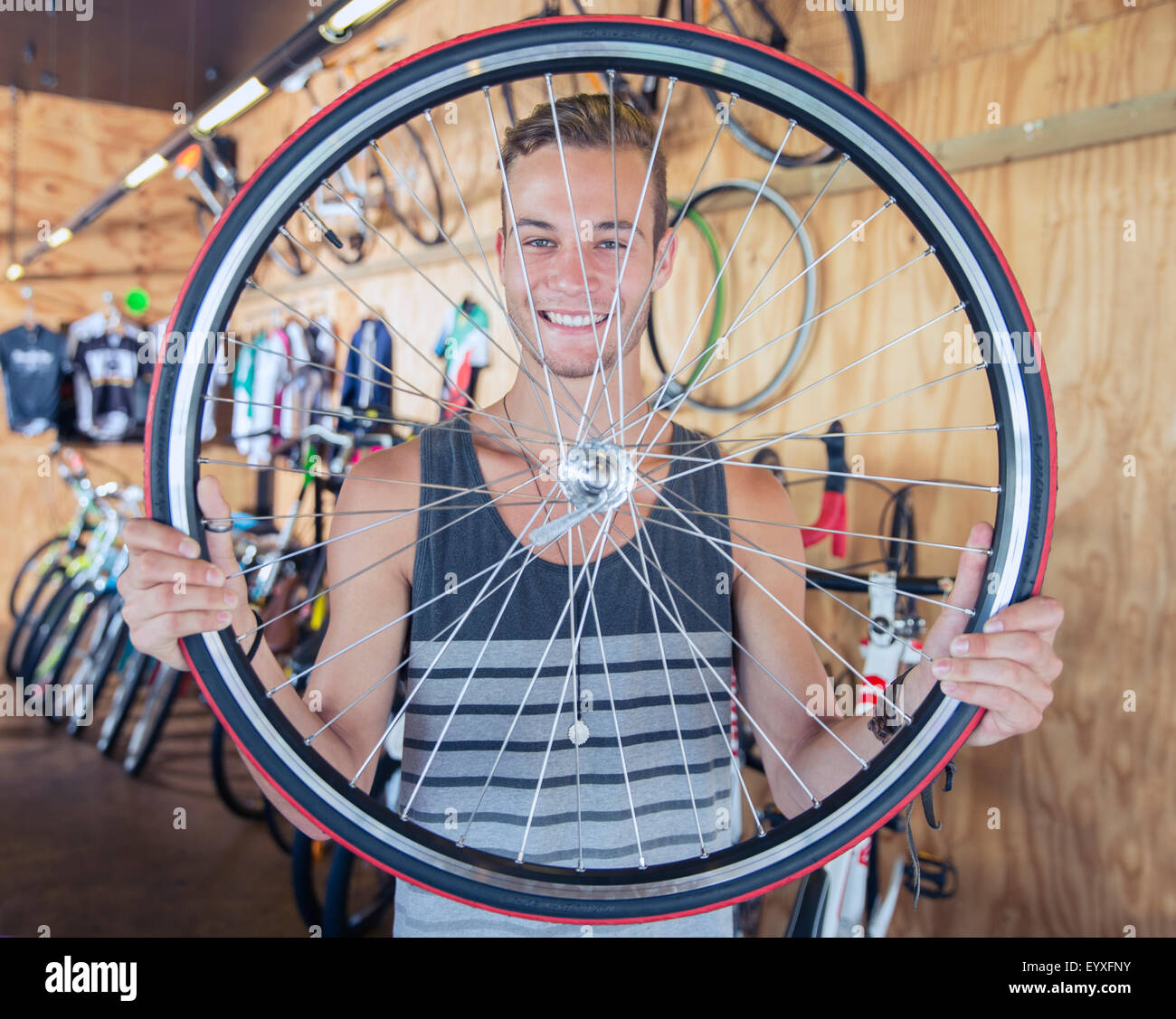 Portrait smiling young man holding bicycle wheel in bicycle shop Stock Photo