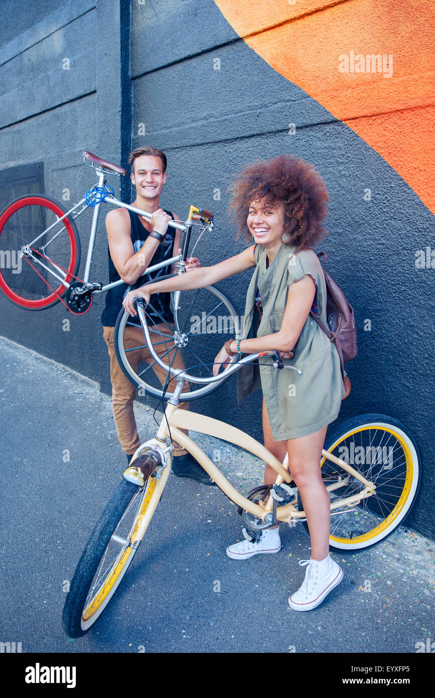Portrait smiling friends with bicycles next to urban wall Stock Photo