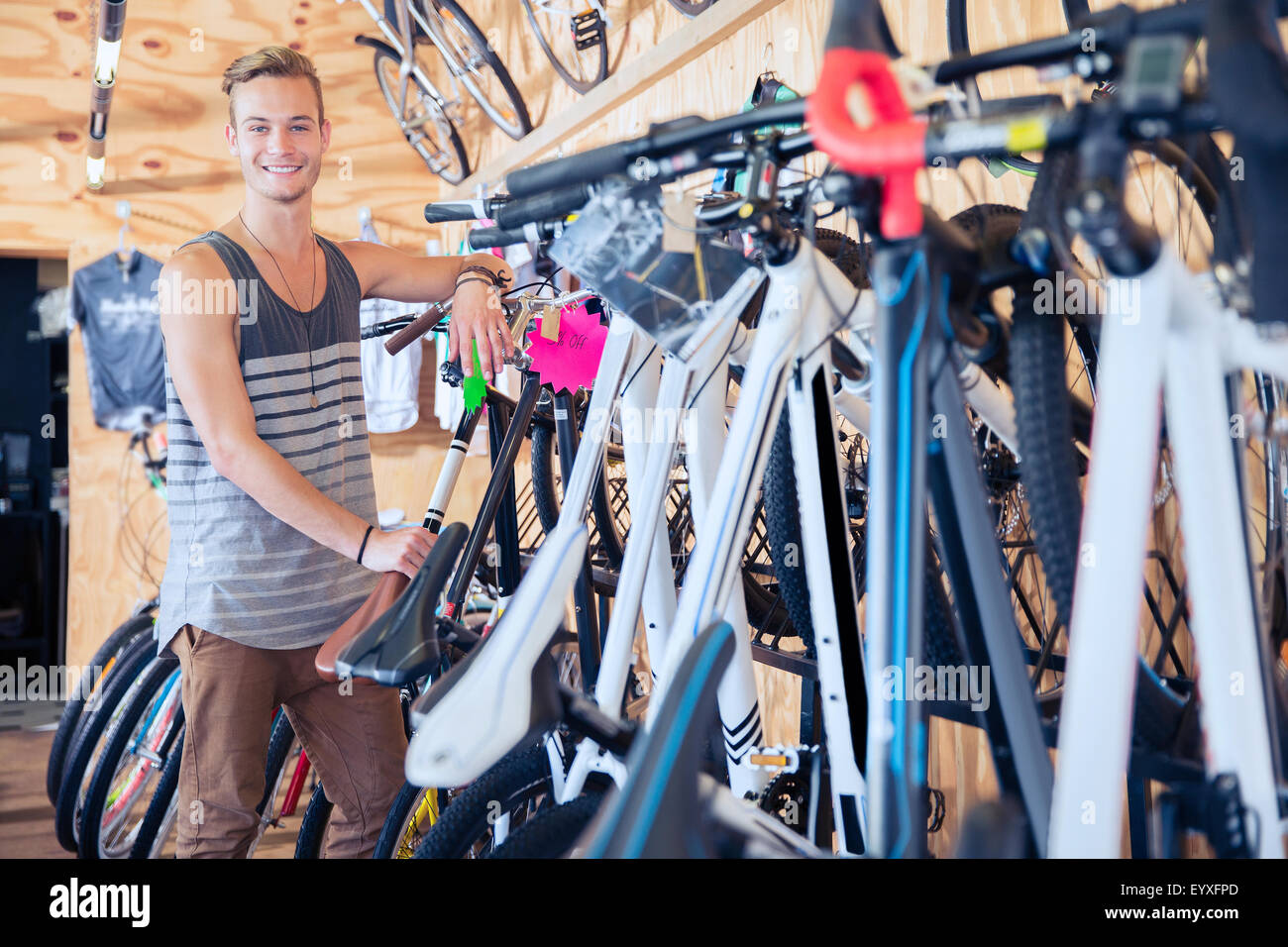 Portrait smiling young man leaning on rack in bicycle shop Stock Photo
