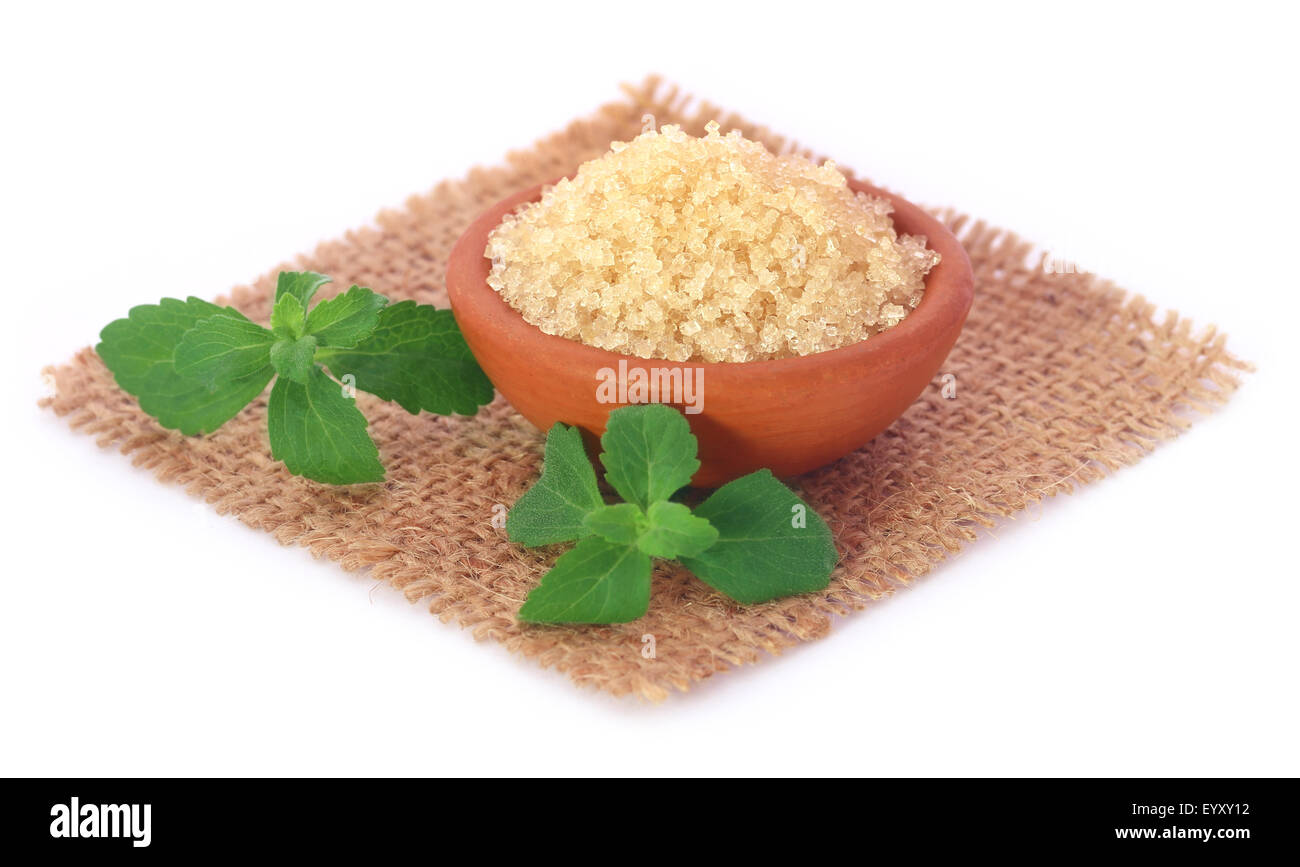Coarse crystals of brown sugar with stevia leaves over white background ...