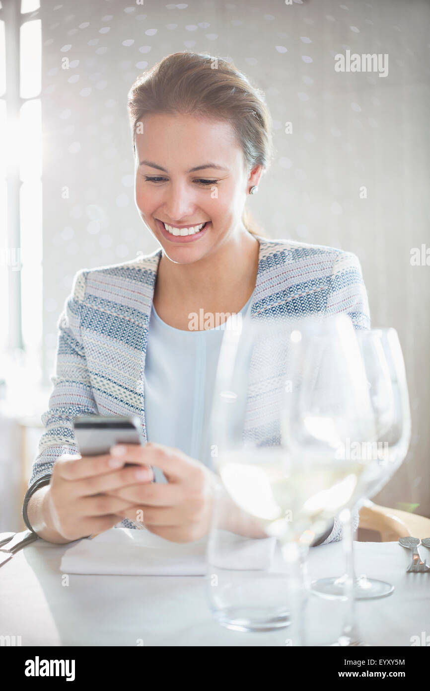 Smiling woman texting with cell phone at restaurant table Stock Photo