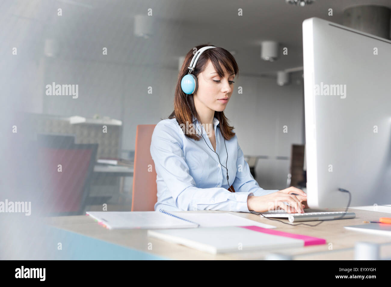 Brunette businesswoman with headphones working at computer in office ...