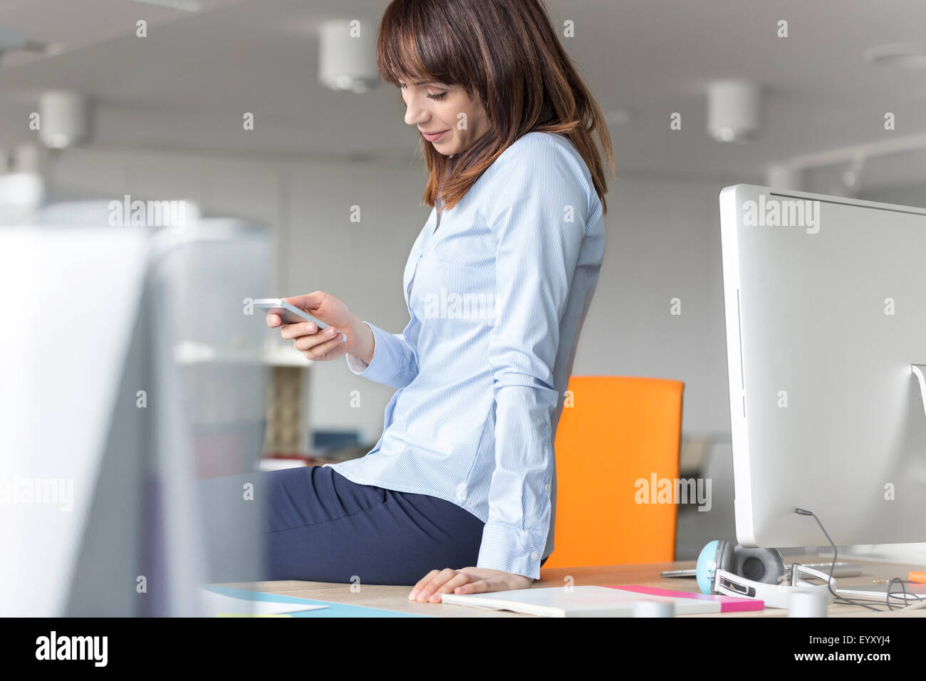 Brunette businesswoman texting with cell phone on desk in office Stock Photo