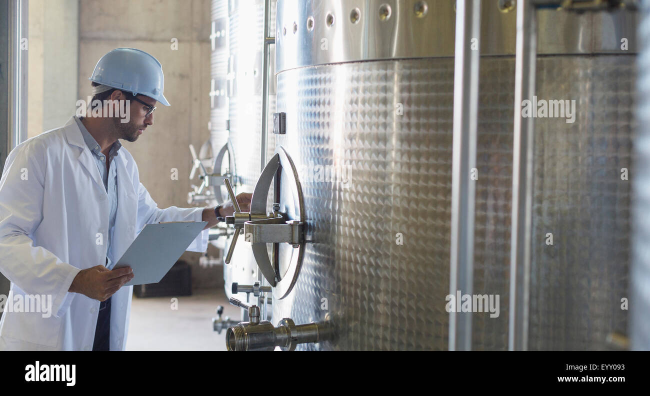 Vintner in lab coat and hard hat examining stainless steel vat in