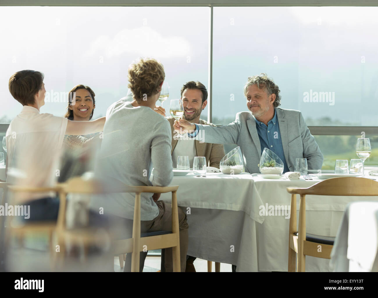 Friends toasting wine glasses at sunny restaurant table Stock Photo