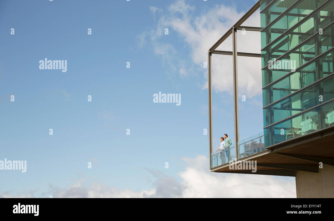 Men standing on balcony of glass bump out against blue sky Stock Photo