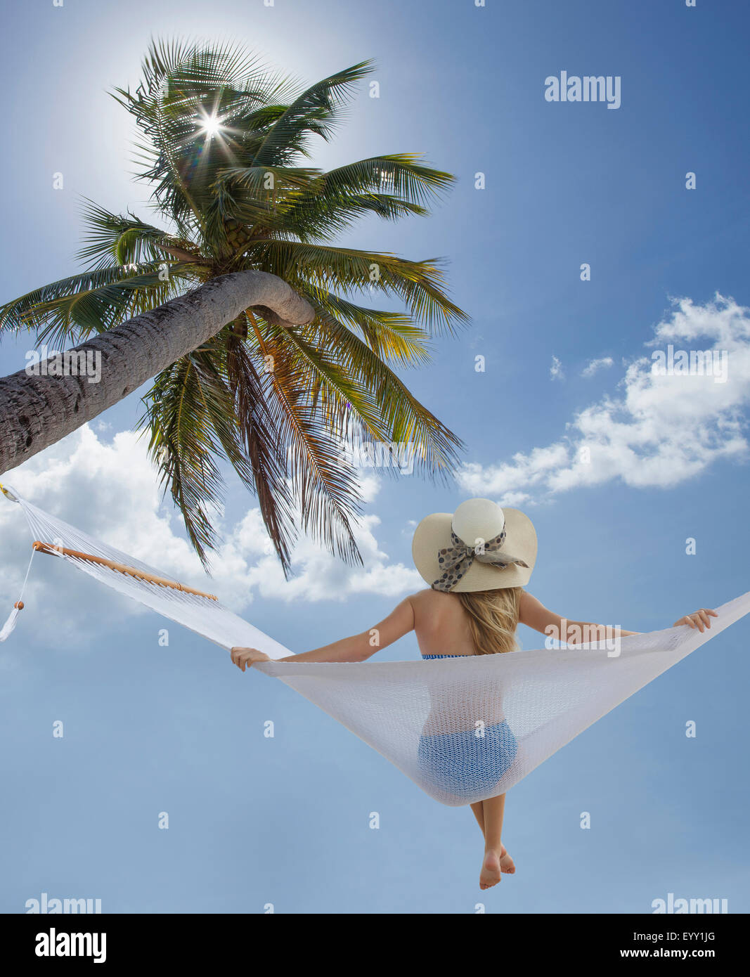 Caucasian woman sitting in hammock under palm tree Stock Photo