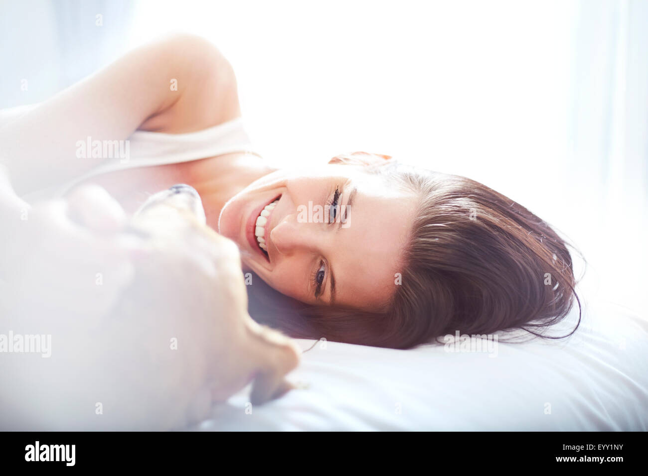 Smiling woman laying on bed with dog Stock Photo