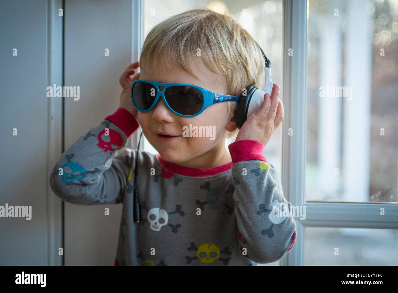 Caucasian boy wearing headphones and sunglasses indoors Stock Photo