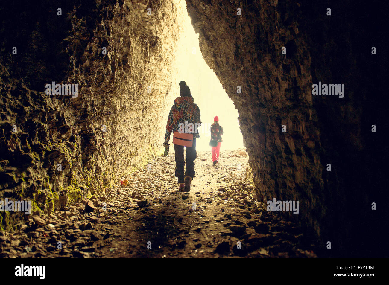 Caucasian hikers walking in rocky cave Stock Photo