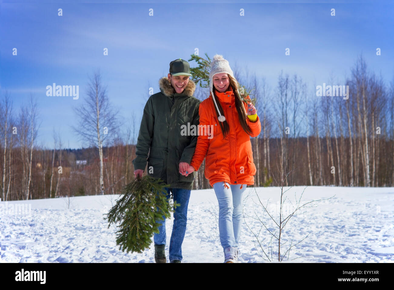 Caucasian couple carrying tree branch in snowy field Stock Photo
