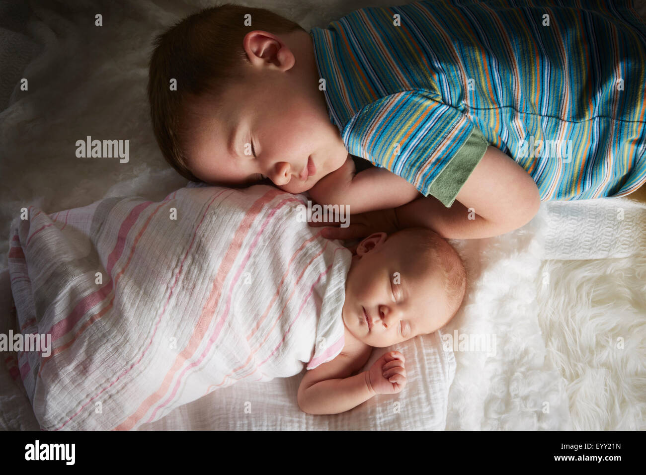 Boy napping with newborn sibling on bed Stock Photo