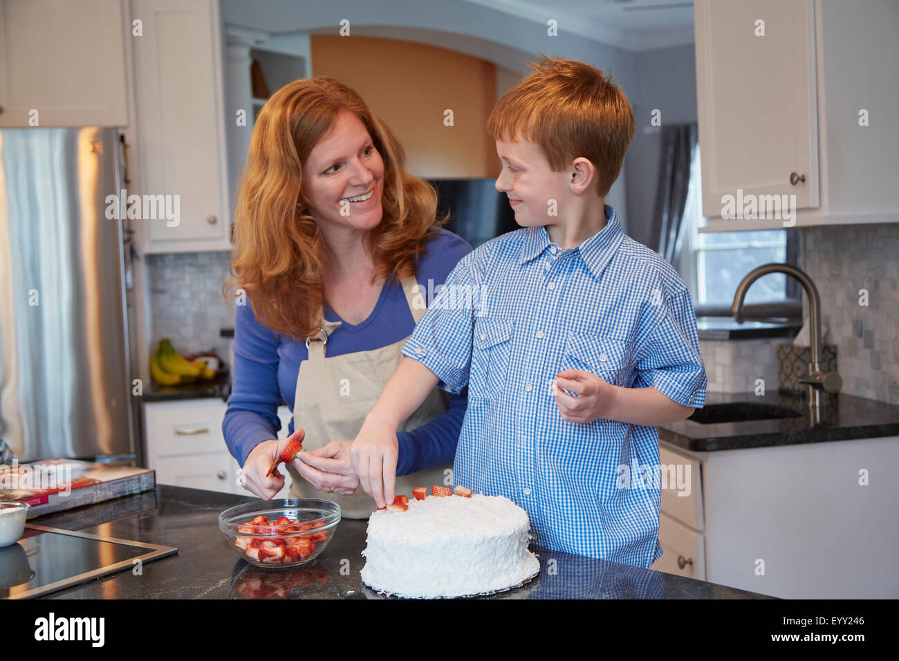Caucasian mother and son decorating cake in kitchen Stock Photo