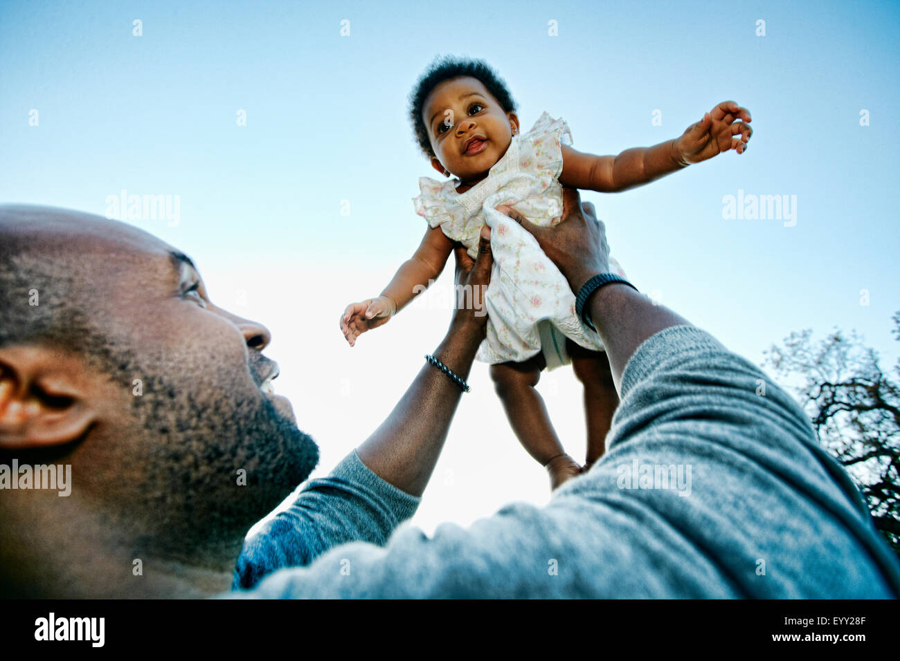 Black father holding baby daughter under blue sky Stock Photo