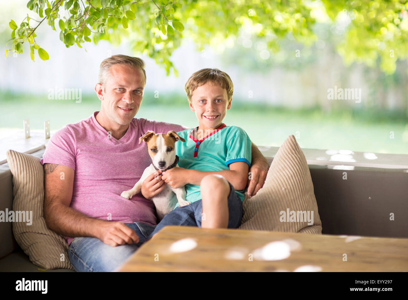 Caucasian father and son sitting with dog on sofa Stock Photo