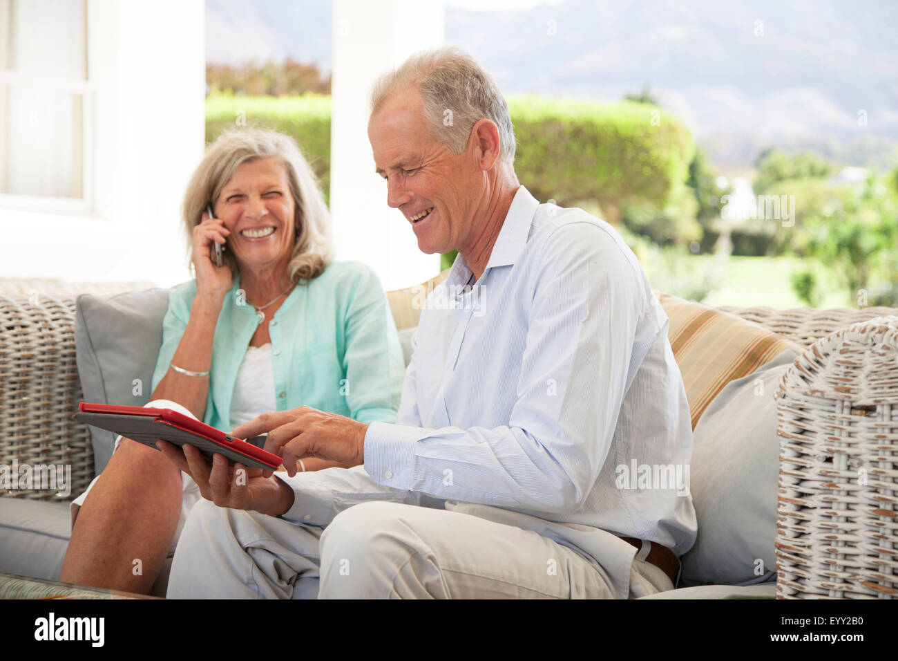 Caucasian couple using cell phone and digital tablet on sofa Stock Photo