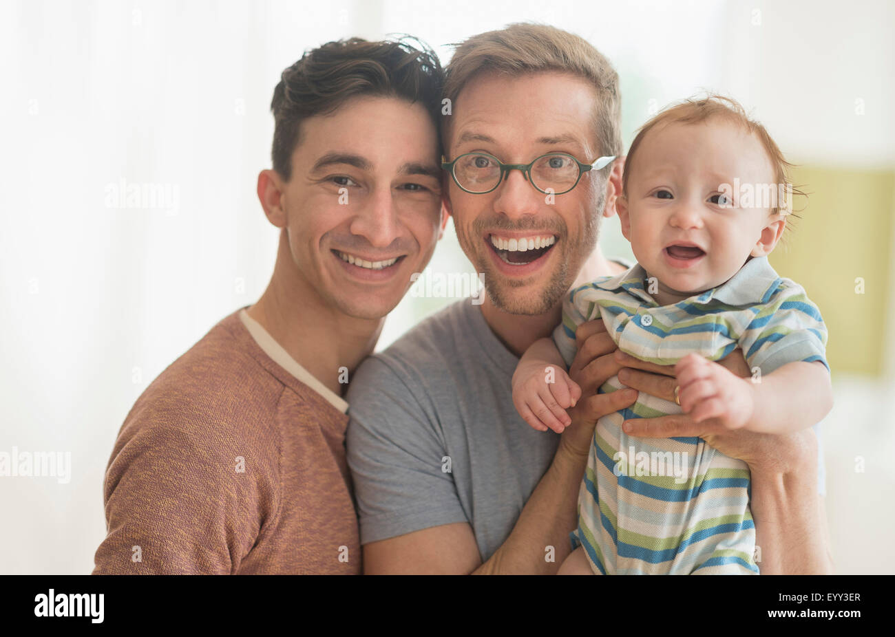 Smiling Caucasian gay fathers holding baby Stock Photo