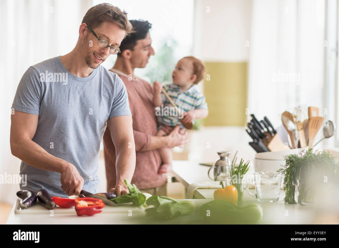 Caucasian gay fathers and baby cooking in kitchen Stock Photo