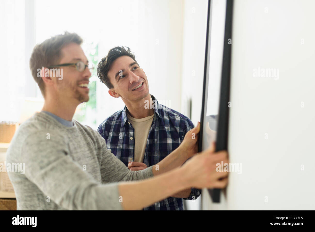 Caucasian gay couple hanging picture on wall Stock Photo
