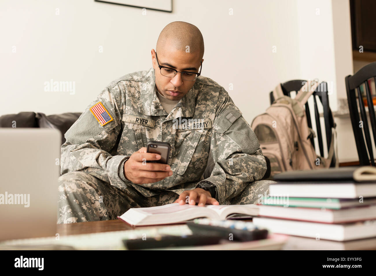Mixed race soldier texting on cell phone and studying on sofa Stock Photo