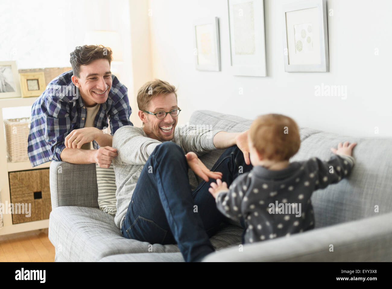 Caucasian gay fathers and baby relaxing on sofa Stock Photo