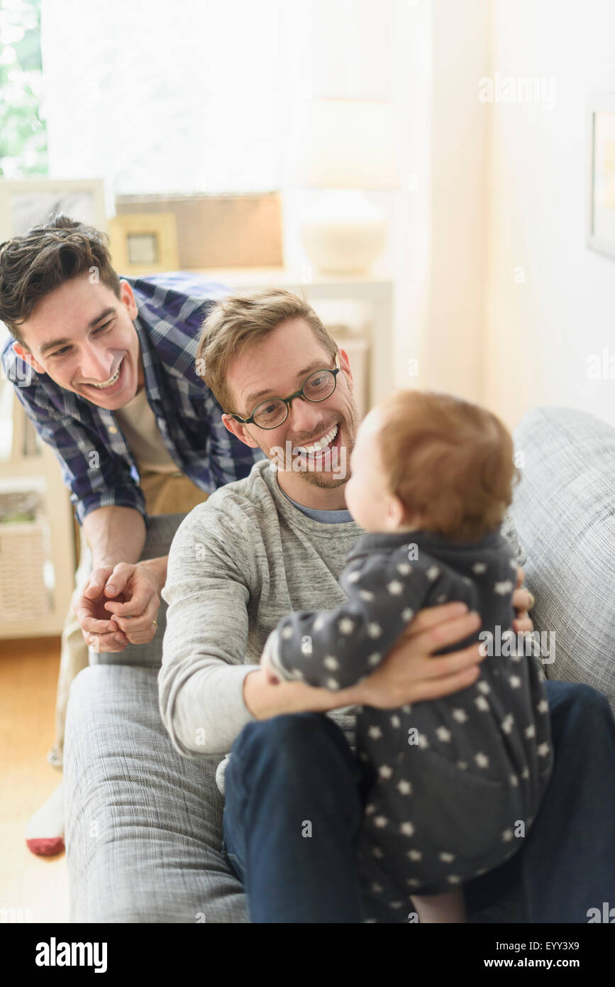 Caucasian gay fathers and baby relaxing on sofa Stock Photo