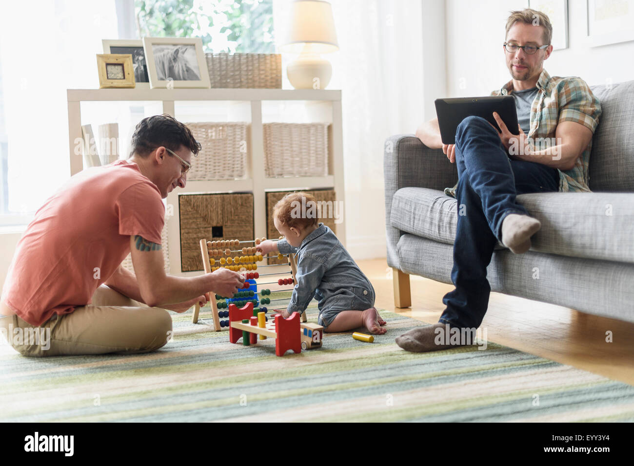 Caucasian gay fathers and baby relaxing in living room Stock Photo