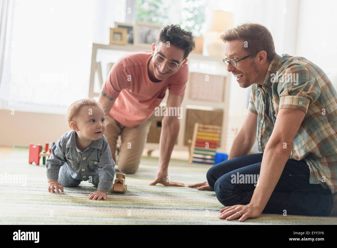 Caucasian gay fathers and baby playing in living room Stock Photo