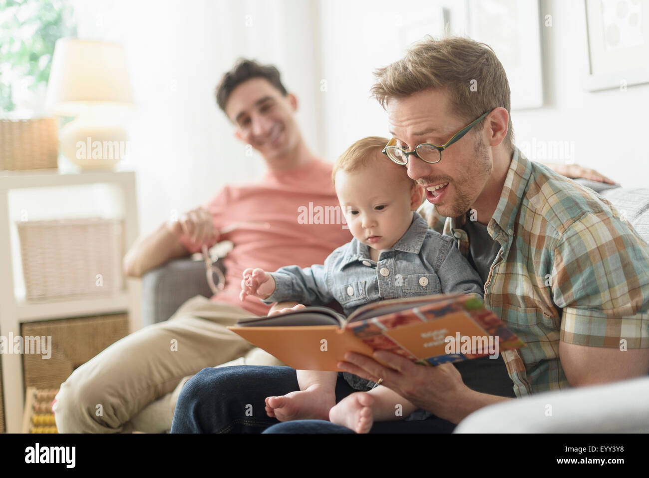 Caucasian gay fathers reading to baby in living room Stock Photo