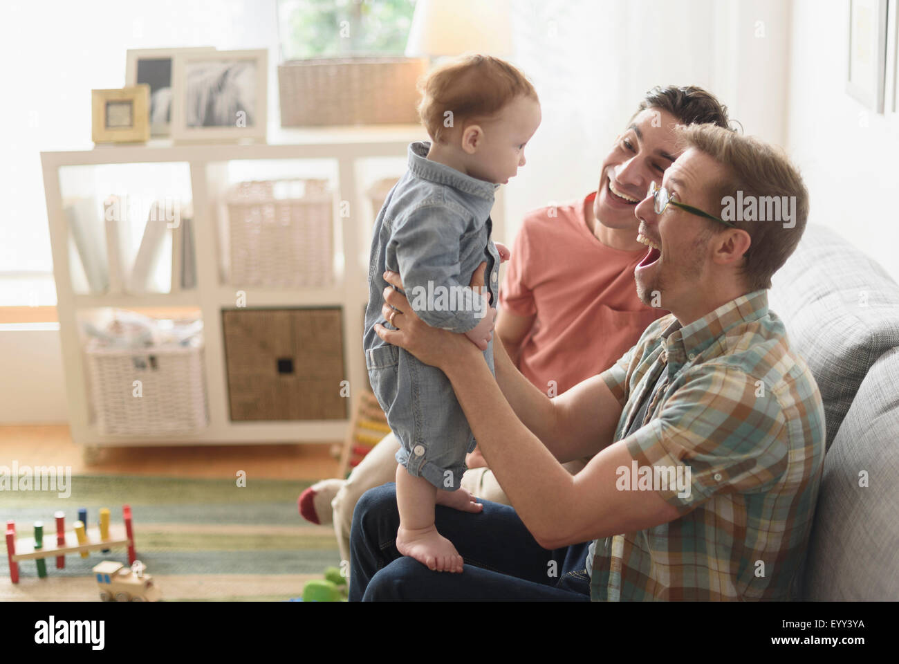 Caucasian gay fathers and baby playing in living room Stock Photo