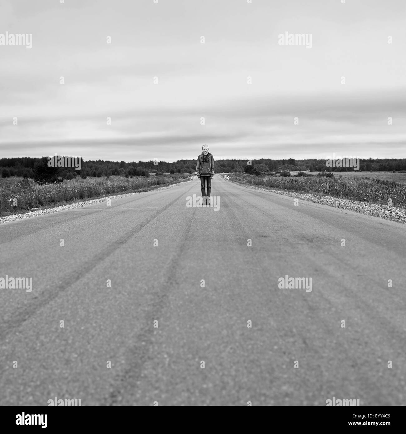 Caucasian girl standing on empty rural road Stock Photo