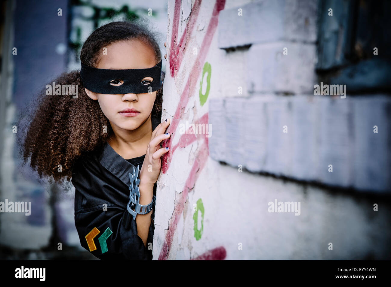Mixed race girl in mask peeking around corner Stock Photo Alamy