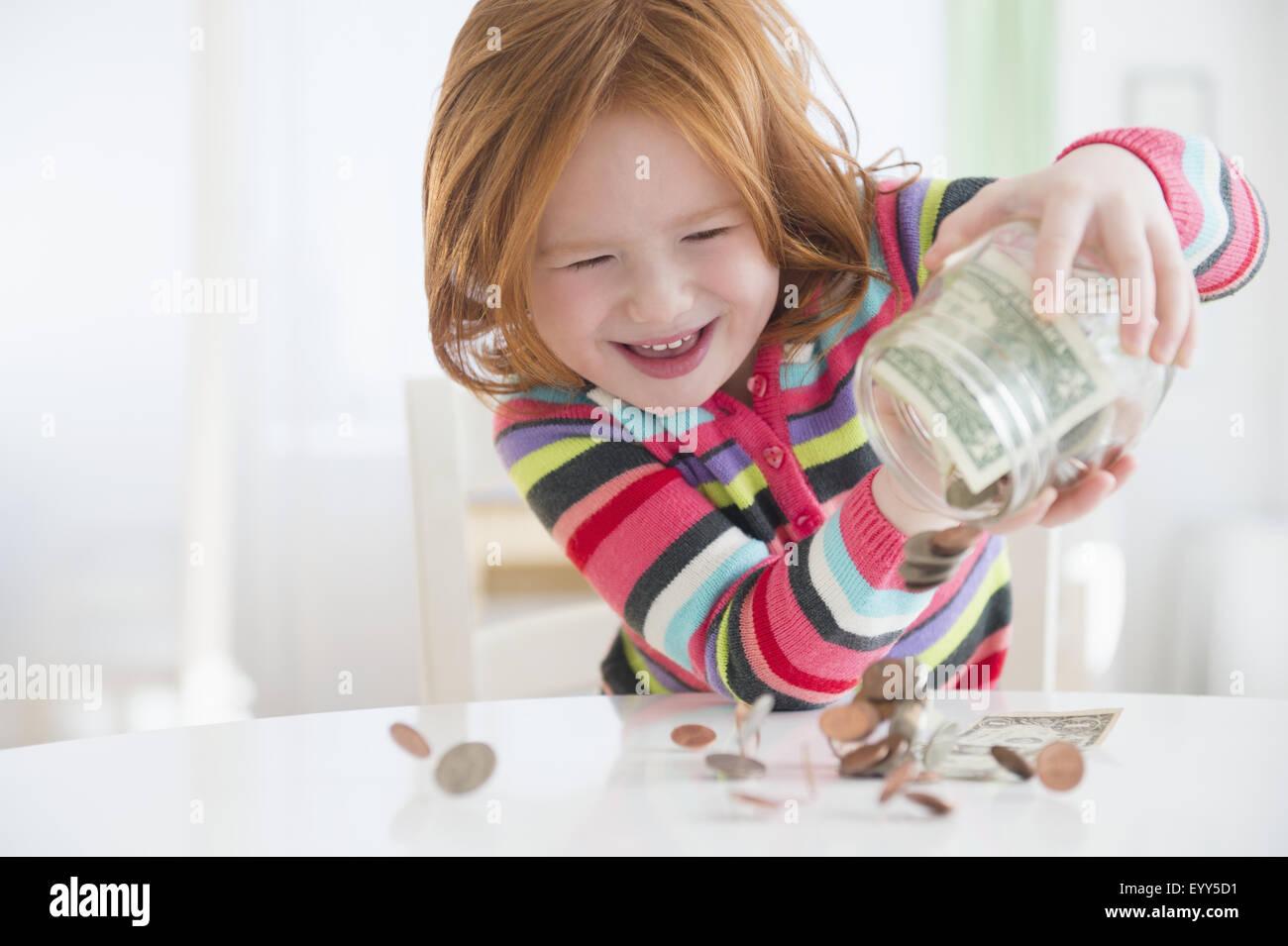 Caucasian girl pouring money from change jar Stock Photo