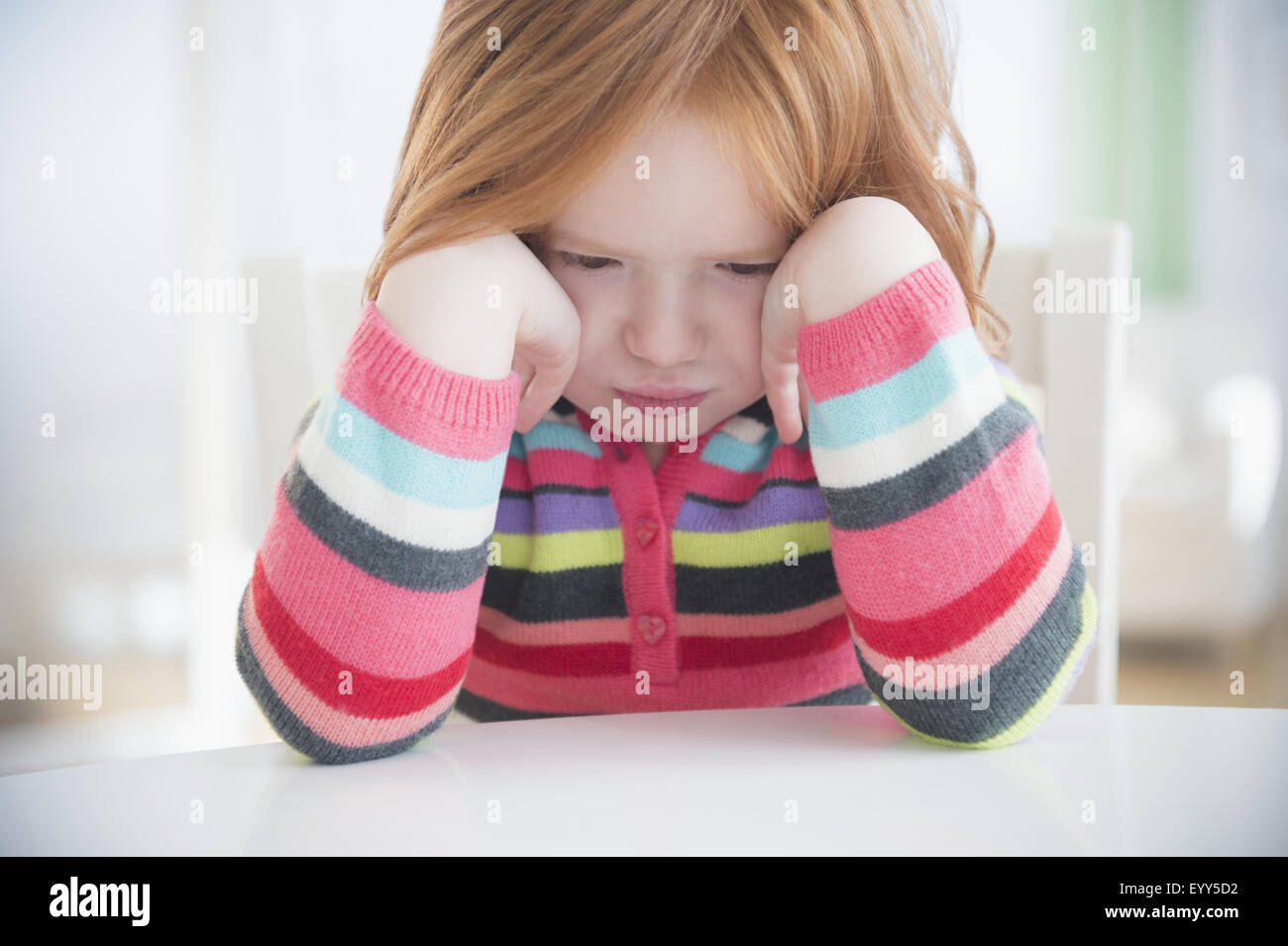 Caucasian girl crying at table Stock Photo