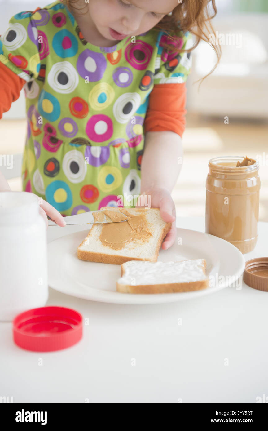 Caucasian girl spreading peanut butter on bread Stock Photo