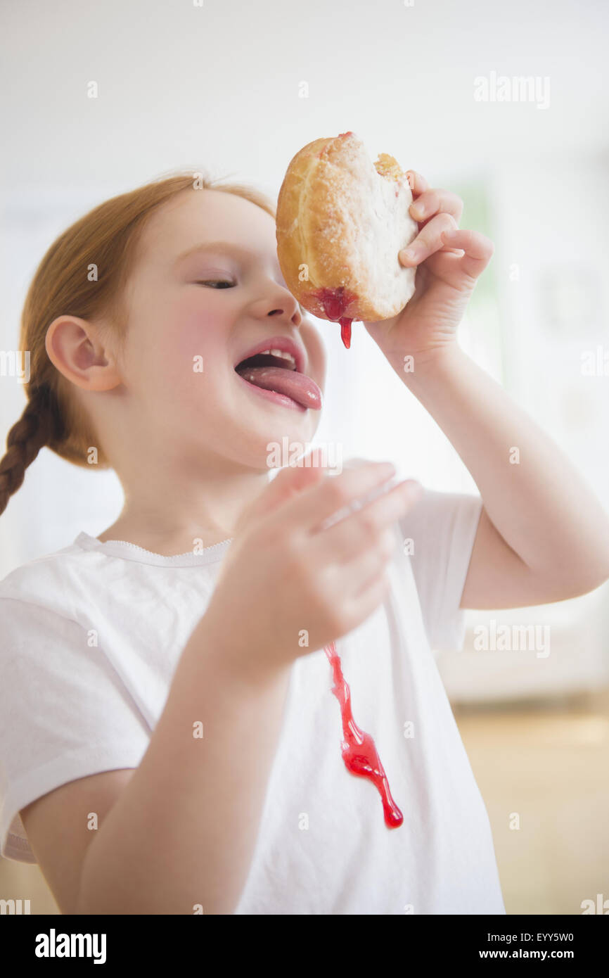 Caucasian girl licking messy jelly donut Stock Photo