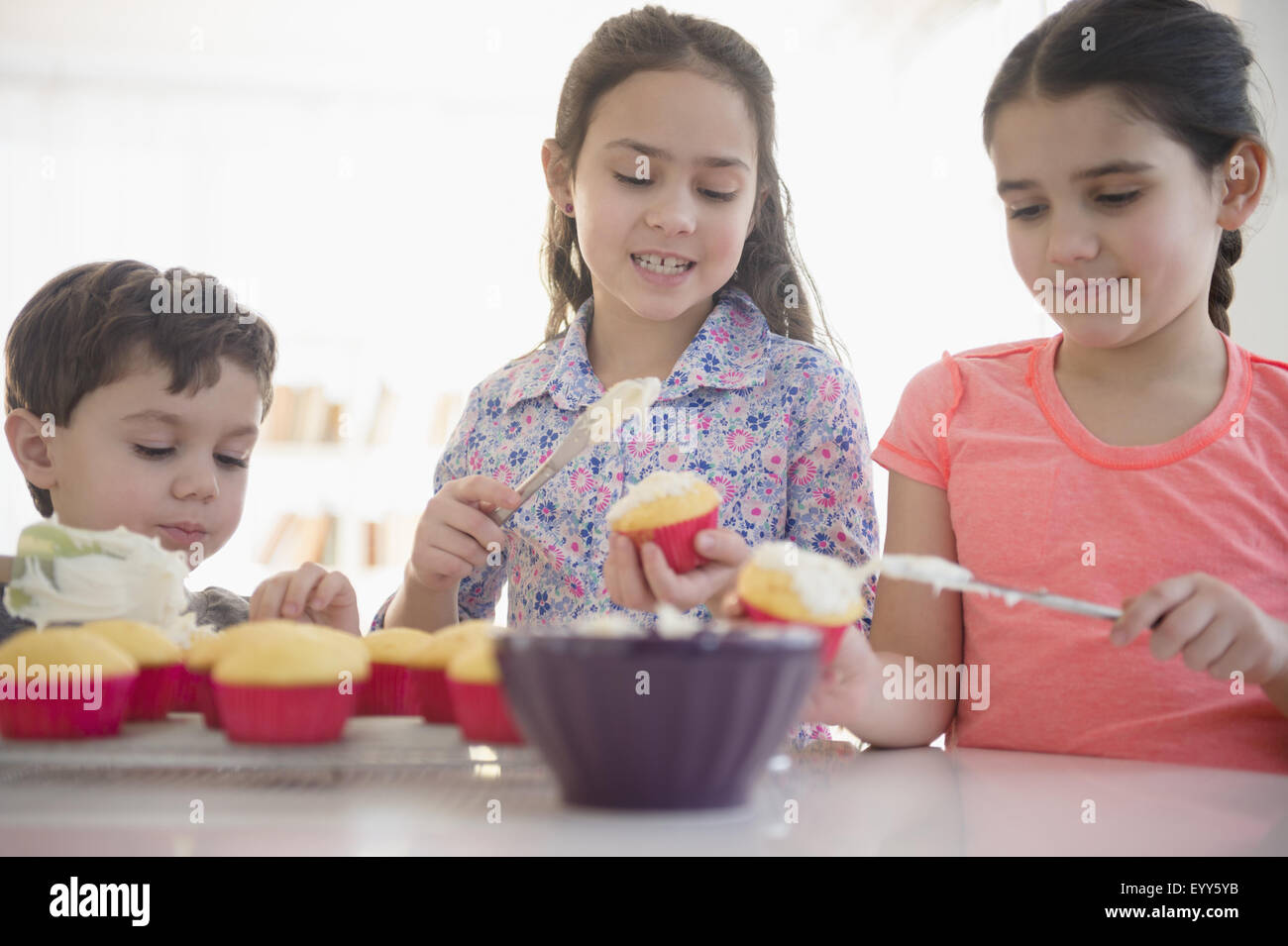 Caucasian siblings spreading frosting on cupcakes Stock Photo
