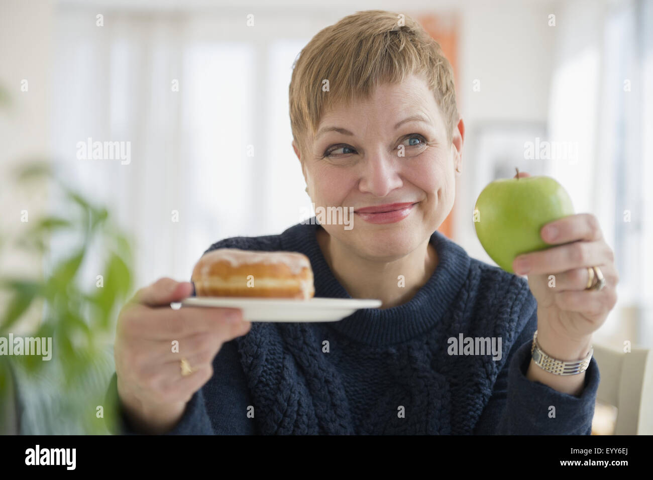 Caucasian woman choosing between donut and apple Stock Photo