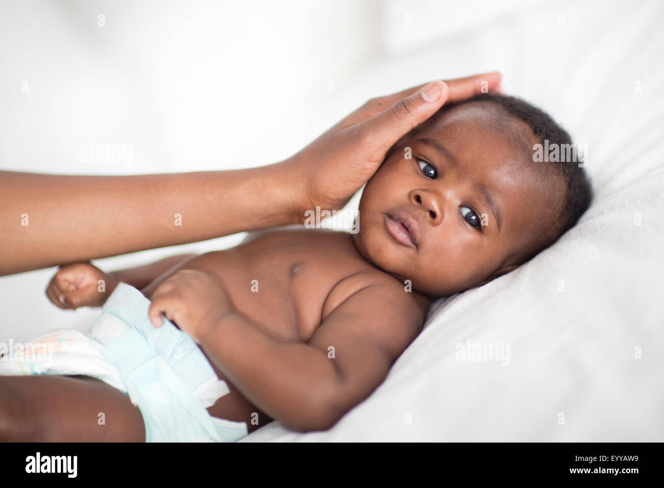 Close up of Black mother patting baby on bed Stock Photo