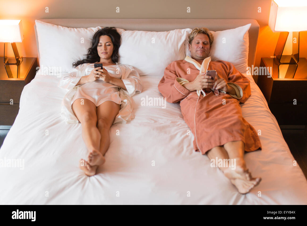 Couple using cell phones on bed Stock Photo