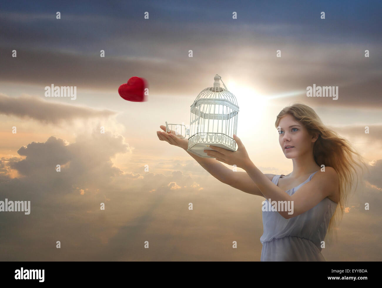 Caucasian woman releasing heart from birdcage Stock Photo