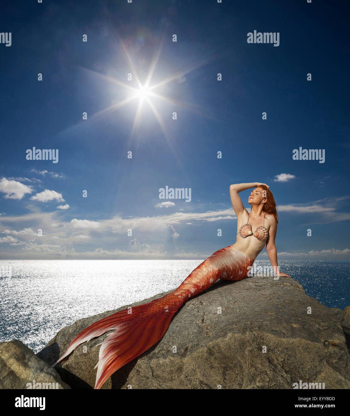 Caucasian mermaid laying on rock near ocean Stock Photo