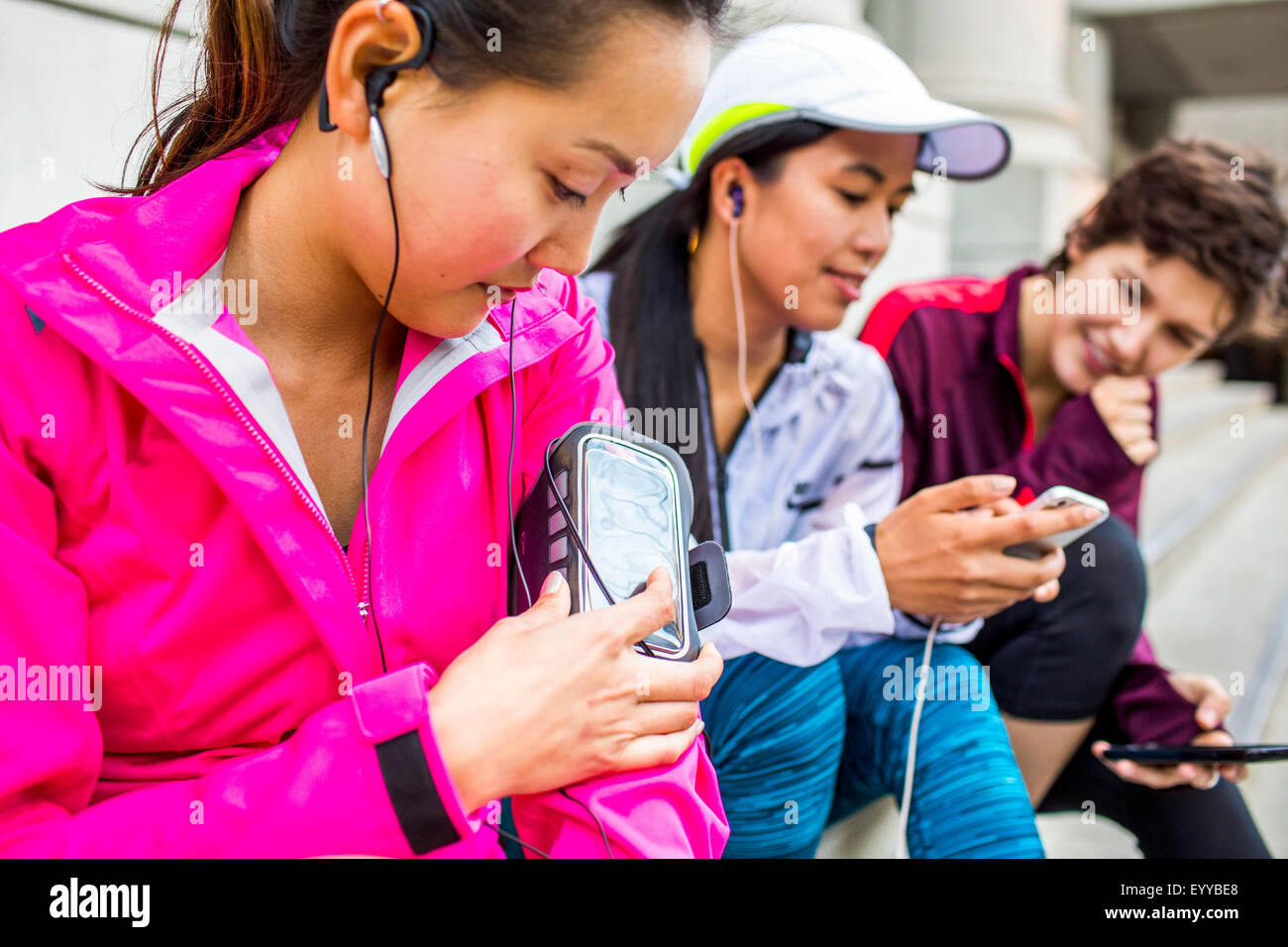 Runners using cell phones and earbud on city sidewalk Stock Photo