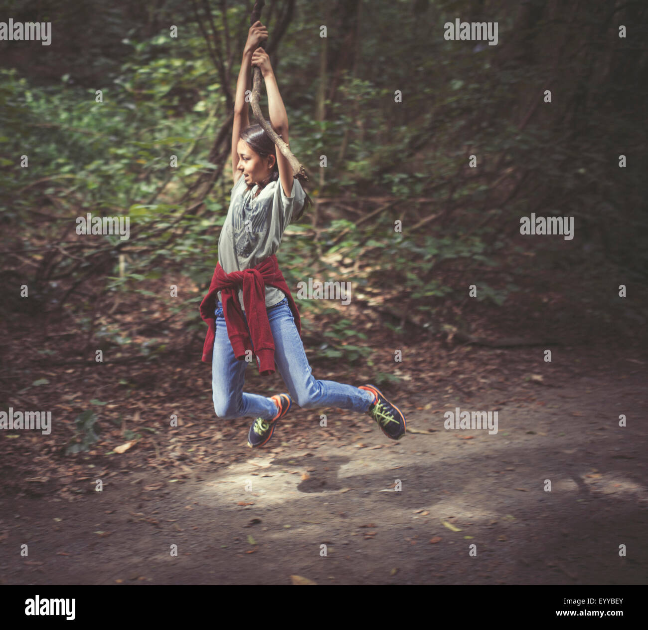 Mixed race girl swinging from tree branch on dirt path Stock Photo