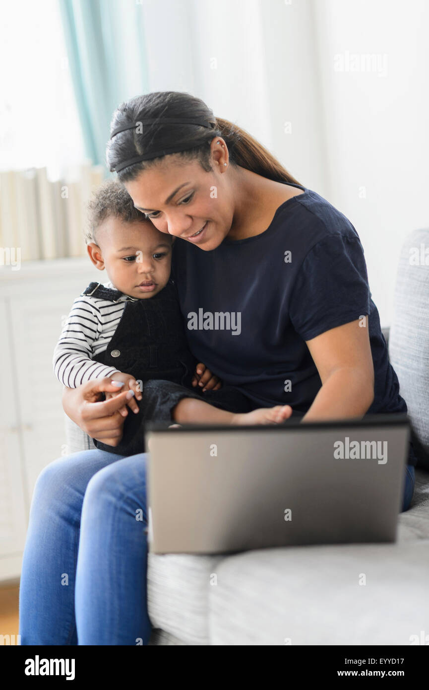 Mixed race mother using laptop with baby son in living room Stock Photo