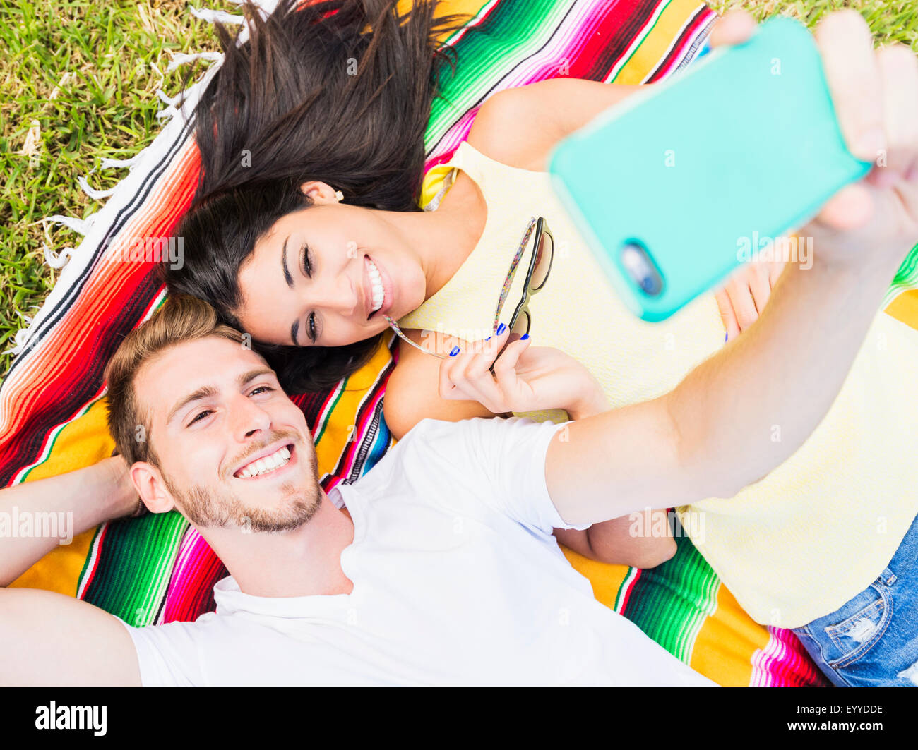 Hispanic couple taking selfie on blanket in park Stock Photo