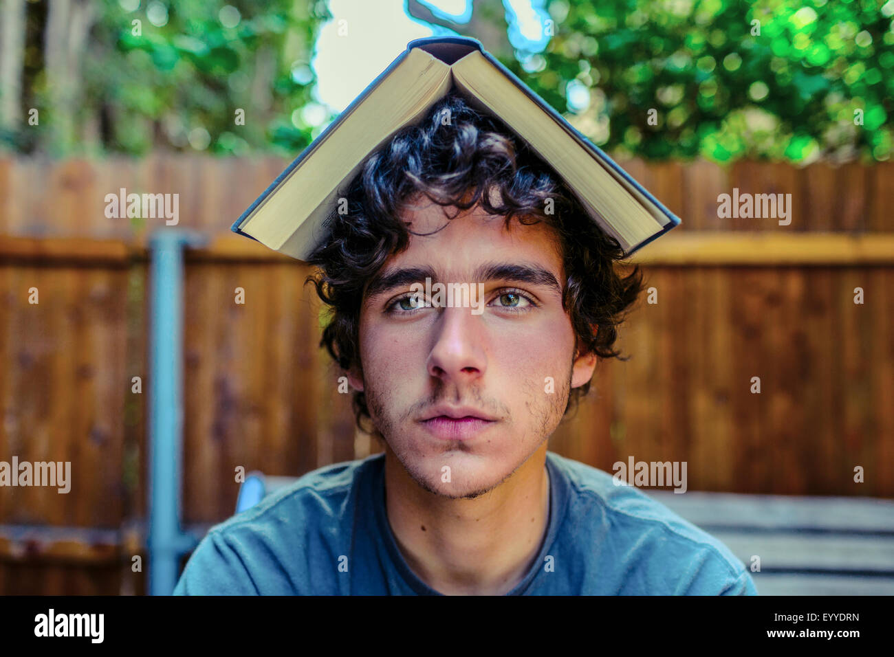 Hispanic man balancing book on head in backyard Stock Photo