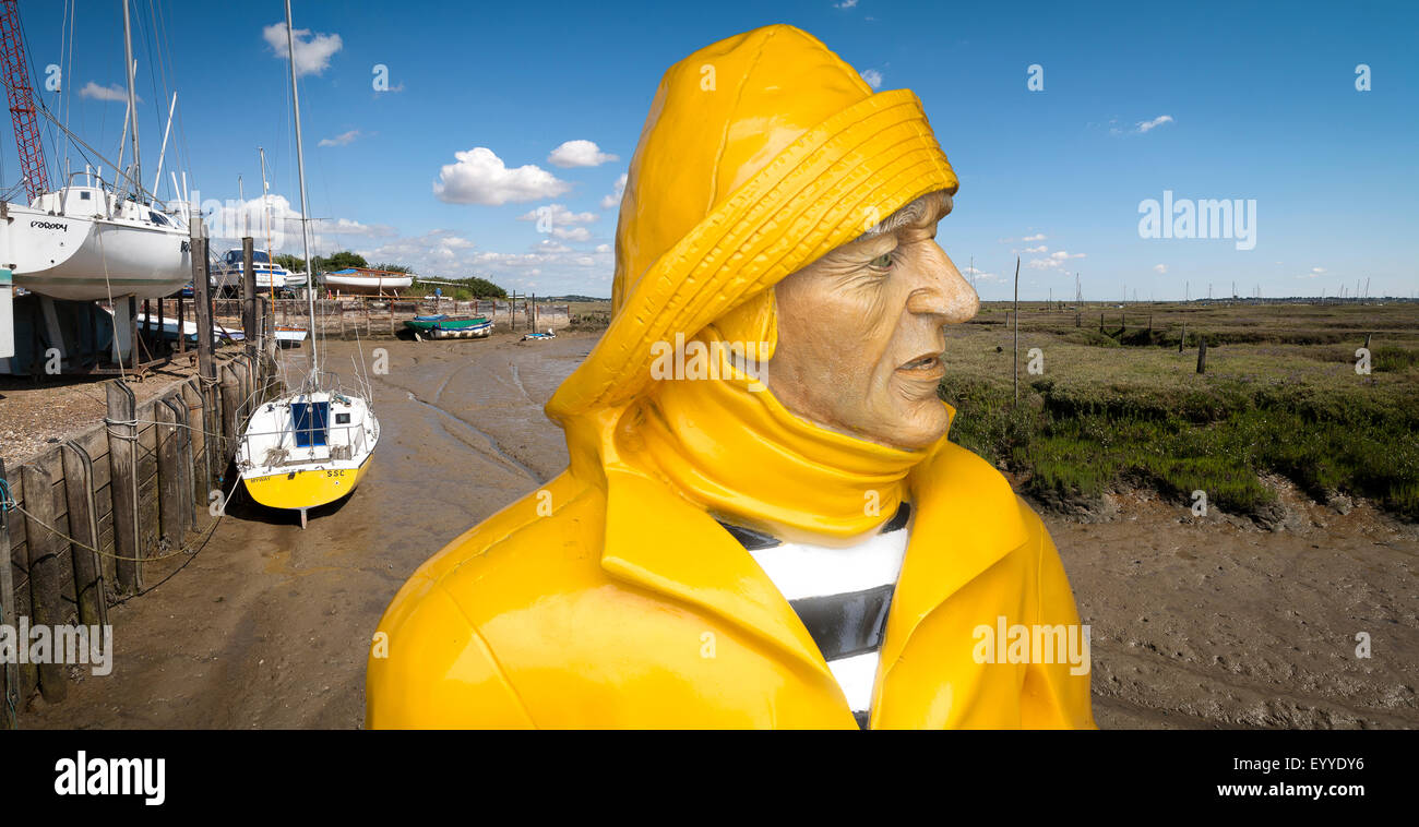 A painted sculpture of a fisherman wearing bright yellow waterproofs and sou'wester manipulated onto an Essex coastline Stock Photo