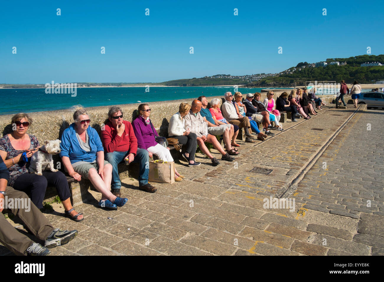 People sunbathing on the harbour wall at St Ives, Cornwall, England, UK Stock Photo